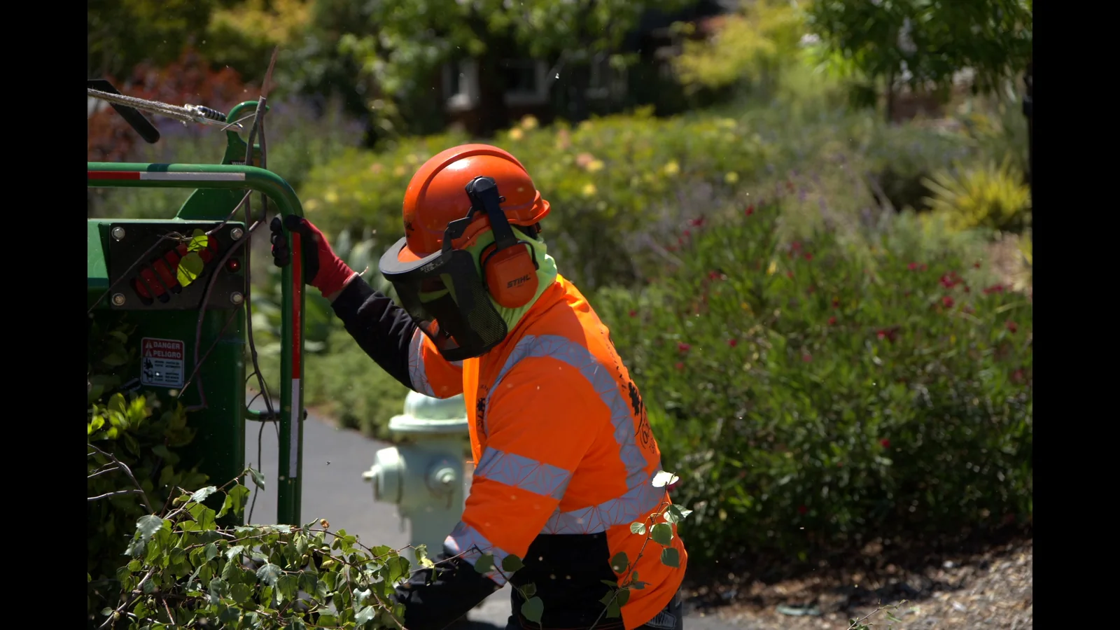 Zambrano crew member in orange PPE feeding branches into a chipper